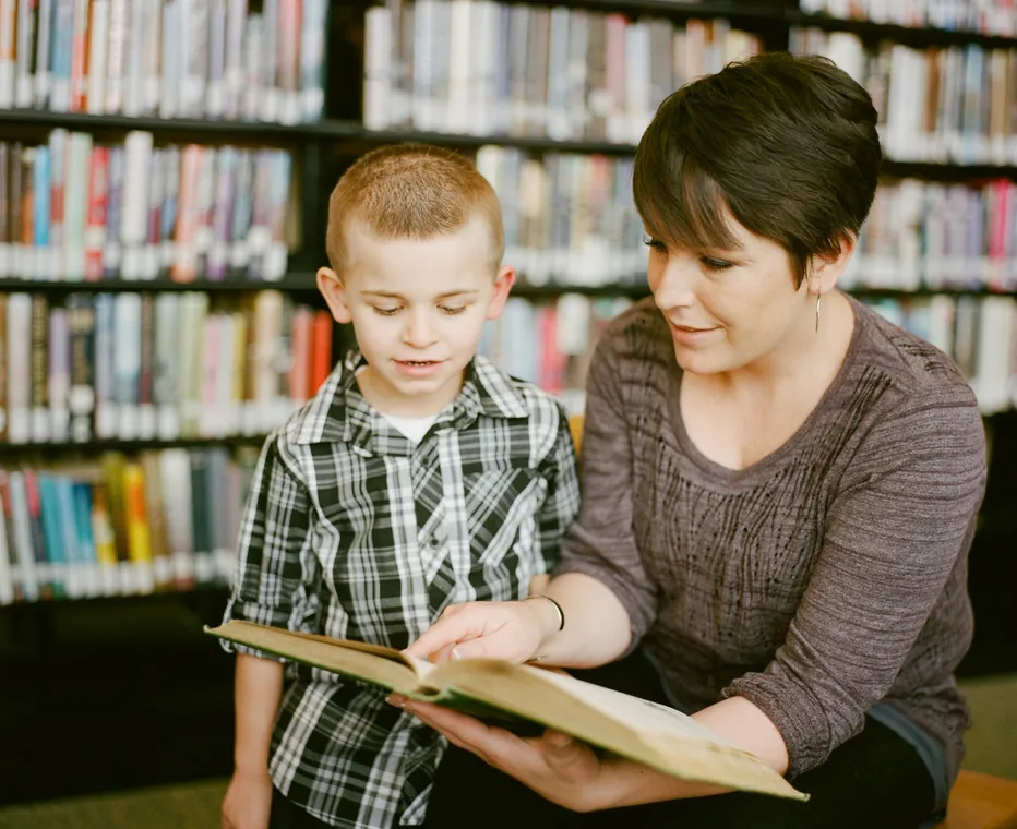 An adult reading a book with a child in a library