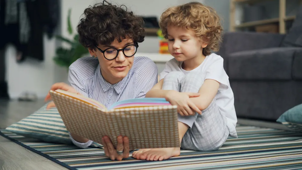 An adult reading a colorful book with a young child at home